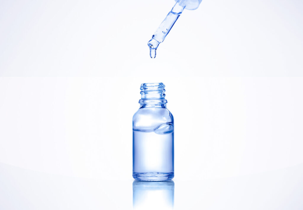 Liquid serum drop from pipette into a cosmetic transparent glass