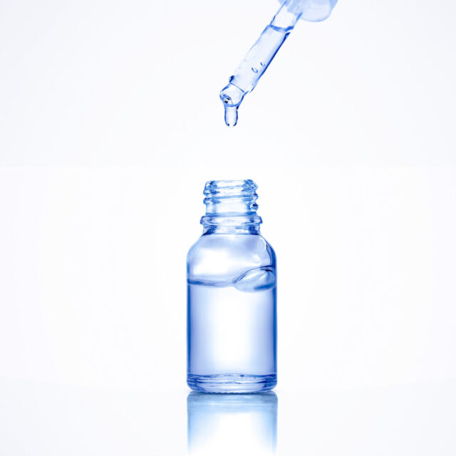 Liquid serum drop from pipette into a cosmetic transparent glass